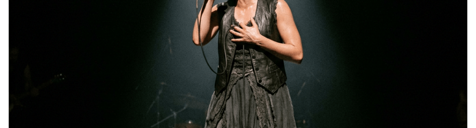 Female singer performing passionately on stage with a microphone under spotlight