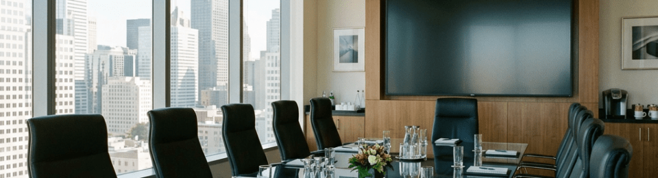 Conference room with large glass table, black leather chairs, notebooks, and water glasses overlooking city skyscrapers