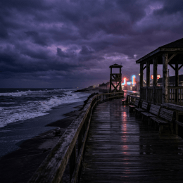 Rainy coastal boardwalk beside rough waves under a dark stormy sky